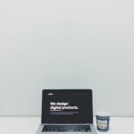 macbook pro beside white and blue plastic cup